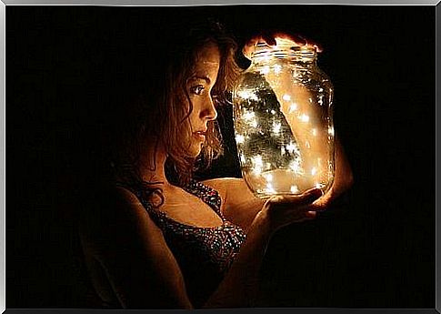 woman holds vase with fireflies in hand