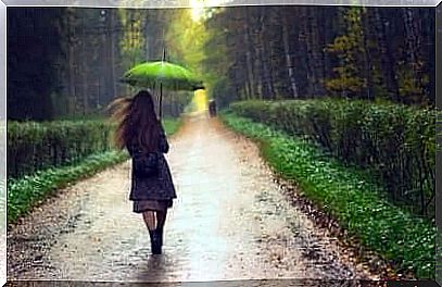 Girl walks in the rain with a green umbrella.