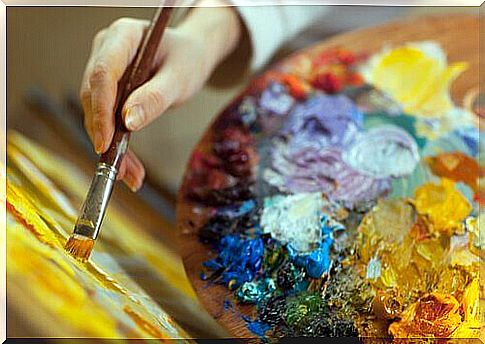 Hand with paintbrush and palette of colors